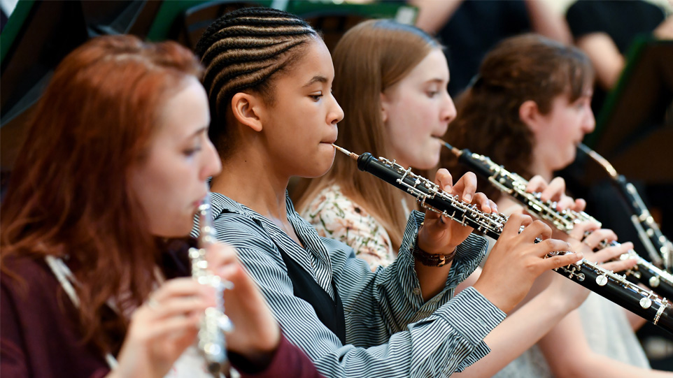 A group of young students, wearing casual clothes, performing on woodwind instruments